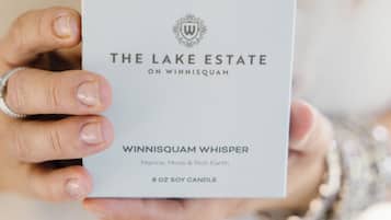 Eine Person hält eine Schachtel, auf der 'The Lake Estate on Winnisquam Whisper 8 oz soy candle' steht.
