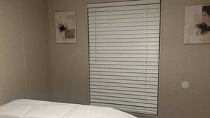 A bedroom with a bed, a window with blinds, and a wall-mounted light fixture. - 3-bedroom mobile home in Florence, SC (Florence)