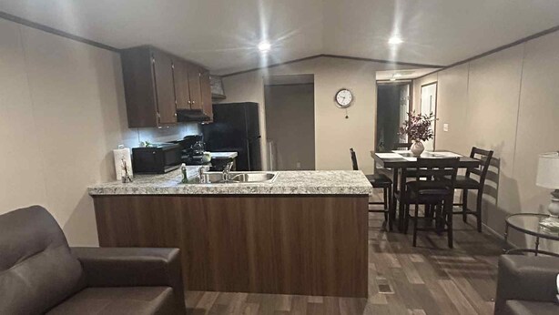 A modern kitchen with a central island, wooden cabinets, and a dining area with a table and chairs. - 3-bedroom mobile home in Florence, SC (Florence)