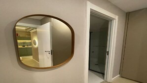Ein Flur mit einem runden Spiegel an der Wand, einer Tür, die ins Badezimmer führt, und einem Blick auf eine Küche im Hintergrund.