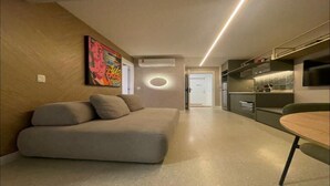 Ein modernes Wohnzimmer mit einer Couch, einem Esstisch und einer Küchenzeile mit integrierten Geräten.