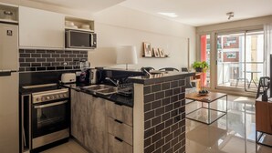Una cuina moderna amb forn integrat, microones i rentatalls, una zona de menjador amb taula de vidre, i vista al balcó exterior.