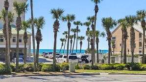 A beachfront hotel with palm trees, parked cars, and a clear view of the ocean.