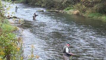 Une rivière où des gens pêchent, entourée de verdure et bordée d’un mur de pierres.