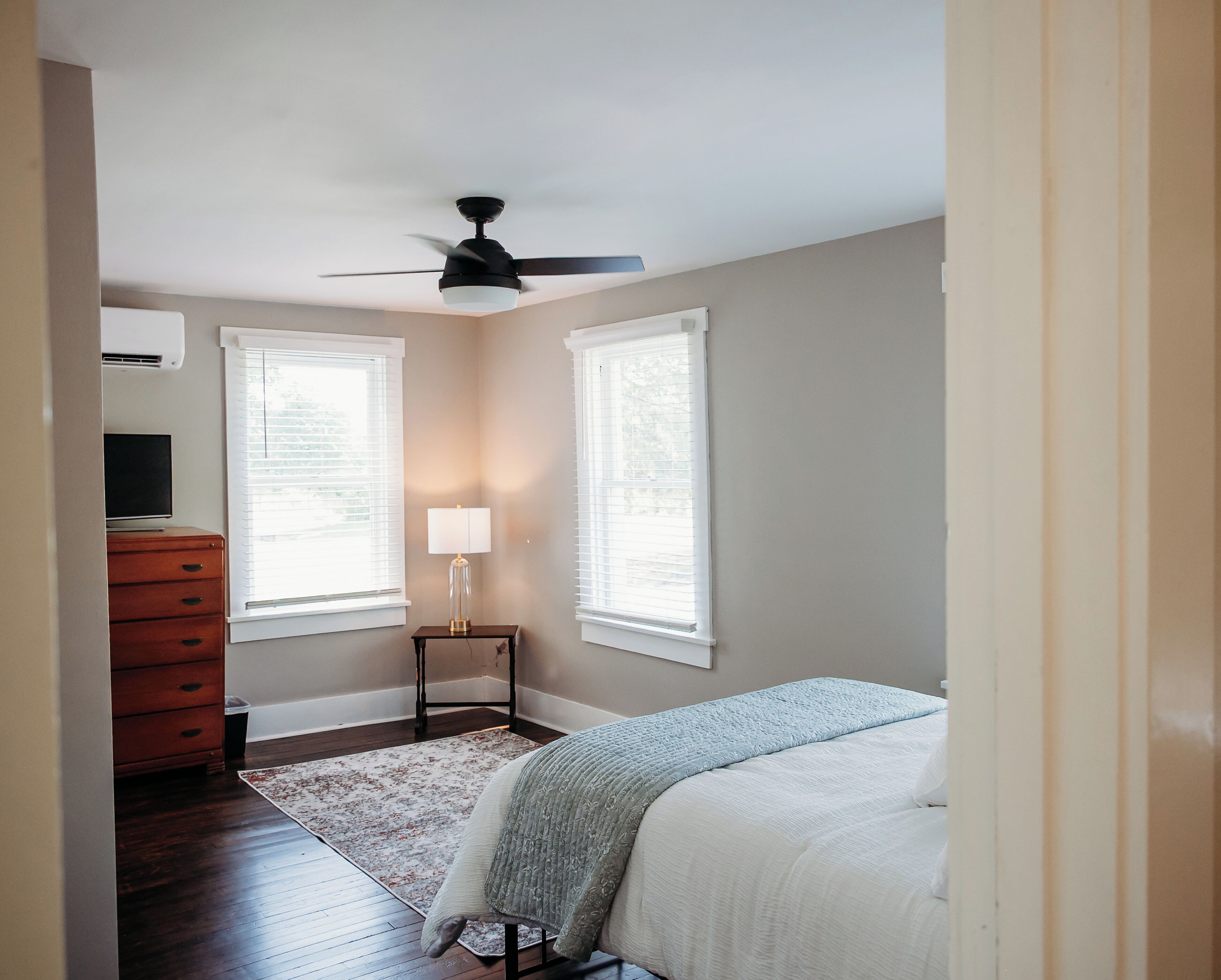Une chambre à coucher comprenant un lit, une table de chevet, une lampe, une commode et un ventilateur de plafond.