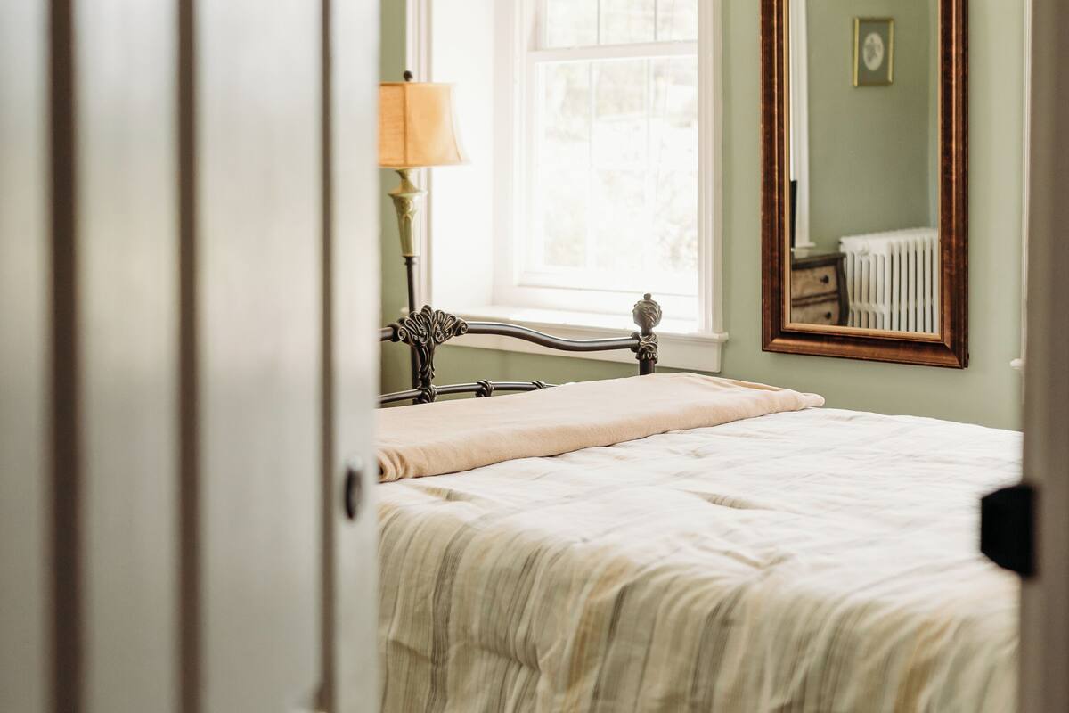 A bedroom with a bed, a window, a lamp, and a mirror.