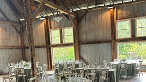 A rustic barn-style venue with wooden beams and large windows, set up for a formal event with round tables and chairs. - Harmony Forge Inn (Milesburg)