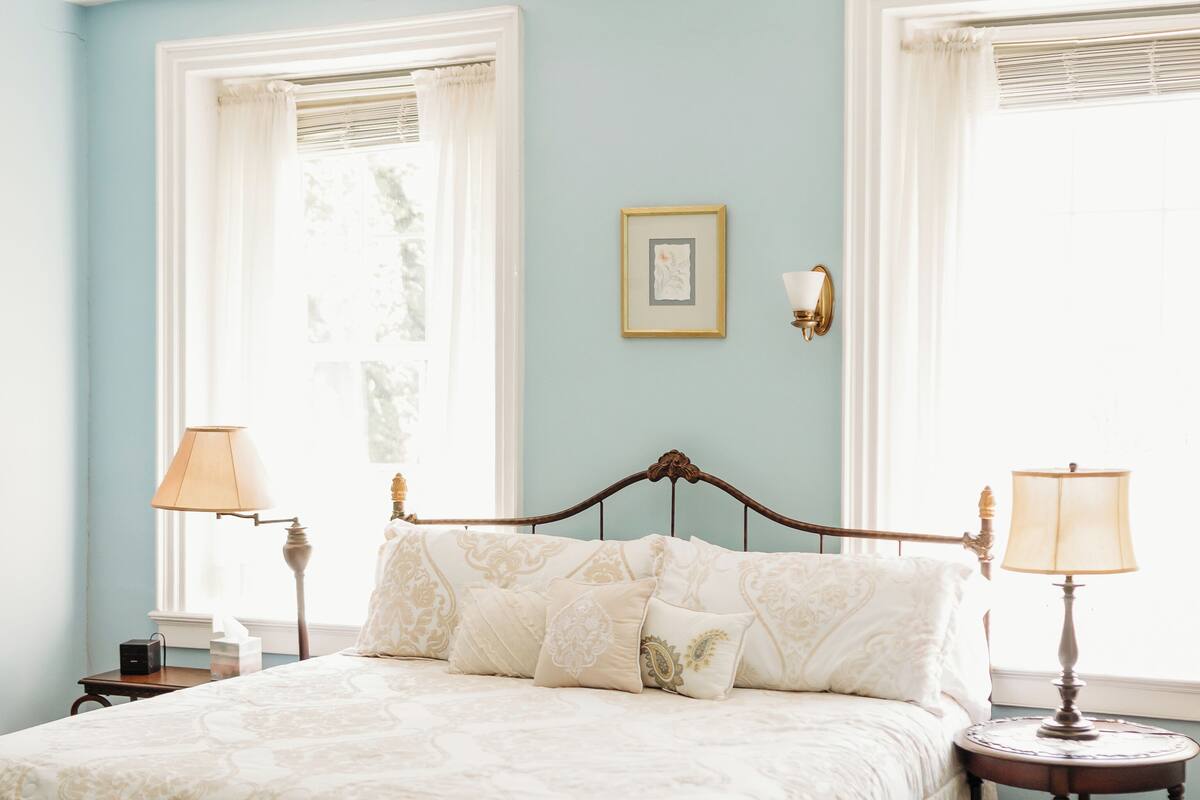 A bedroom with a large bed, two bedside tables, a chair, and a window with curtains.