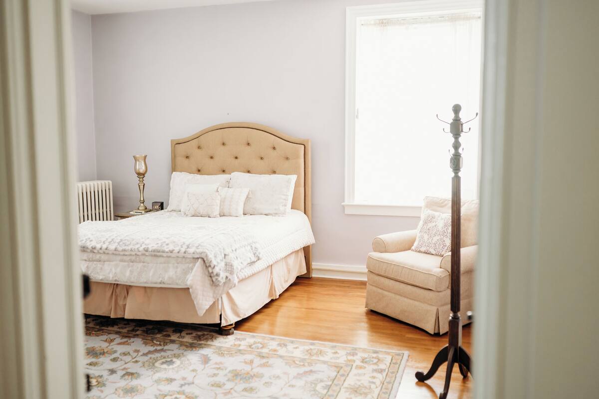 A bedroom with a large bed, a chair, a radiator, and a window.