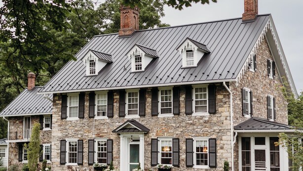 A large stone house with a steep gabled roof, multiple chimneys, and a well-maintained lawn. - Harmony Forge Inn (Milesburg)