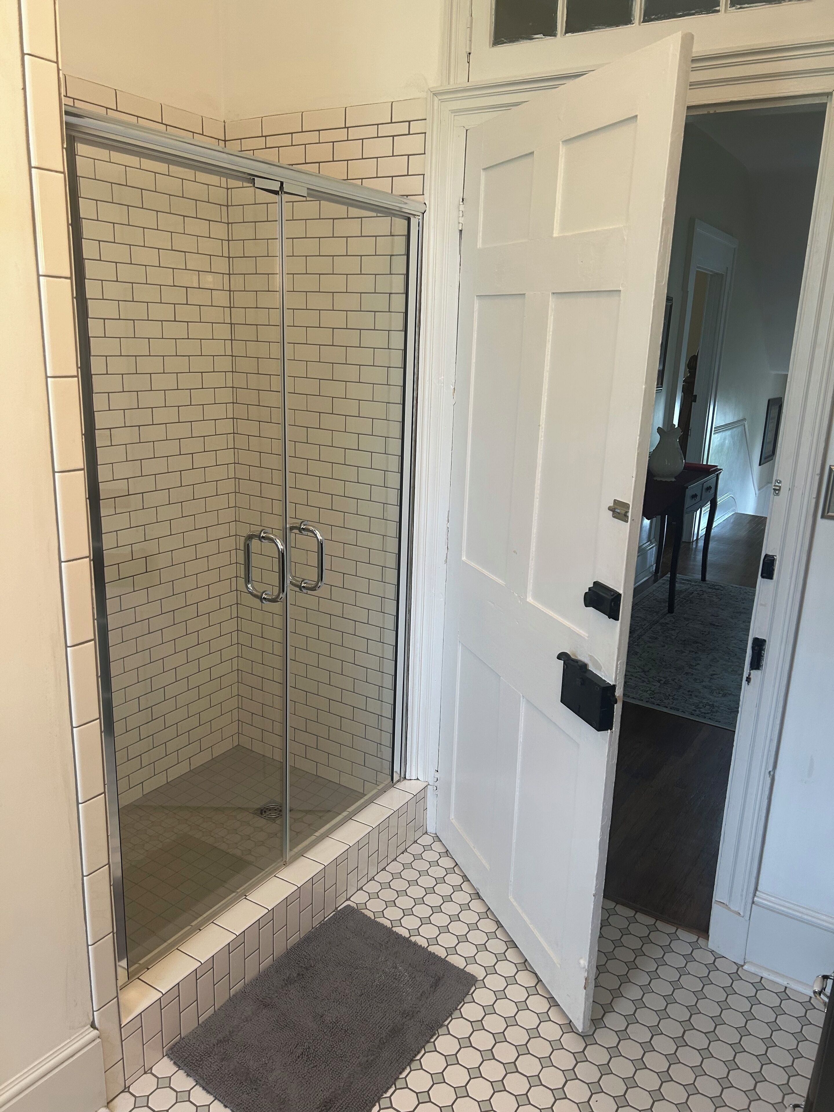 A bathroom with a glass shower enclosure, a white door, and a patterned floor.