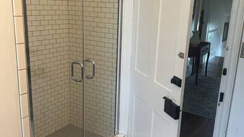 A bathroom with a glass shower enclosure, a white door, and a patterned floor.
