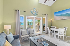 A hotel room with a view of the beach, a dining area, and a living space with a sofa and chairs.