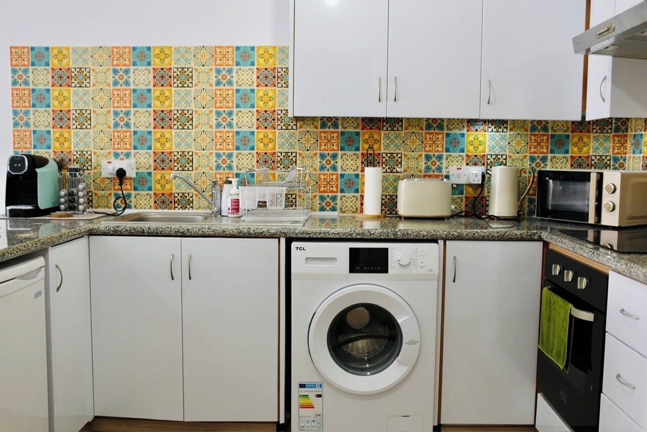 Une cuisine équipée d’un lave-linge, d’un four à micro-ondes et d’un crédence carrelée.