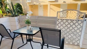 An outdoor patio with a glass table and two chairs, a potted plant, and a decorative fence. - Year-Round Sun! COZY 1BR Studio,Long Stays,Remote Workers,Parking, Paphos center (Paphos)