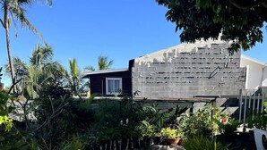 A paved pathway leading to a building with a stone facade, surrounded by lush greenery and palm trees. - La Kaz à Payet (Le Tampon)