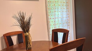A dining area with a round wooden table, four chairs, a vase with dried plants, and an air conditioning unit mounted on the wall.