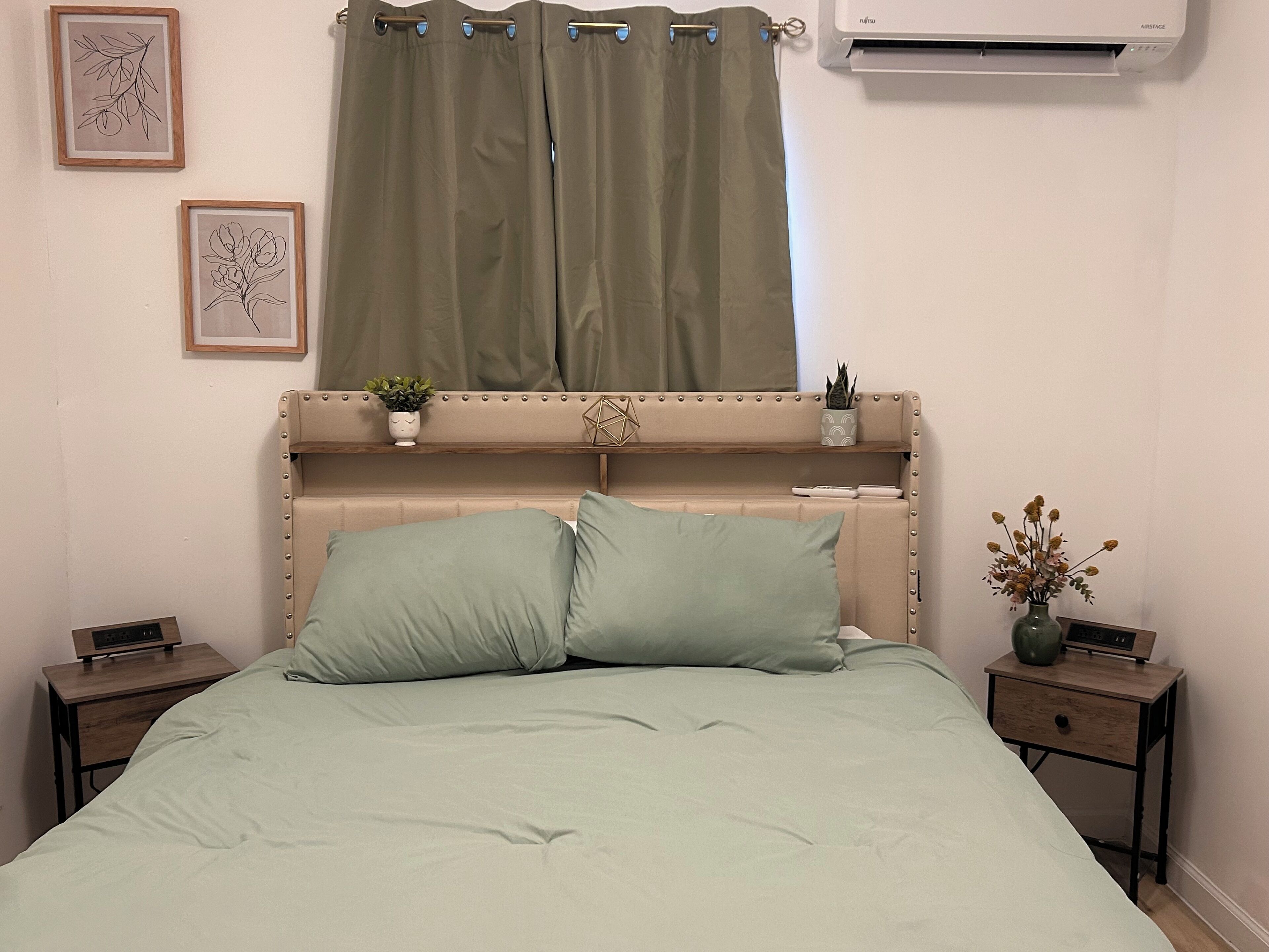 A bed with green bedding, a headboard with decorative elements, a potted plant, and a wall-mounted air conditioner.