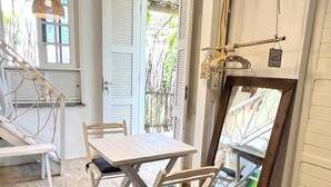 Een eethoek met een tafel en stoelen, een hanglamp en uitzicht door een raam met luiken.