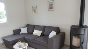 A living room with a grey sectional sofa, a small white table with a plant, and a black wood stove.
