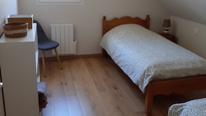 A small, sparsely furnished room with a single bed, a chair, a desk, and a radiator.