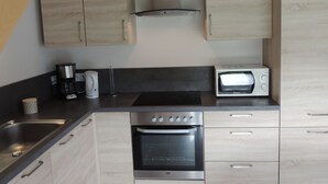 A modern kitchen with light wood cabinets, a stainless steel oven, a microwave, and a coffee maker.
