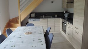 A modern kitchen with wooden cabinets, a dining table with chairs, and a staircase.