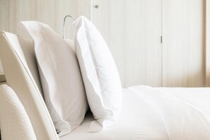 Ein ordentlich bezogenes Bett mit weißer Bettwäsche und Kissen, ein Holfischschrank im Hintergrund und eine Tür rechts.