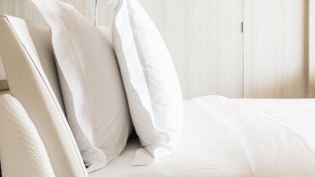 A neatly made bed with white bedding and pillows, a wooden wardrobe in the background, and a door to the right. - Stayspro - Venice Beach Luxury Apartments (Marina del Rey)