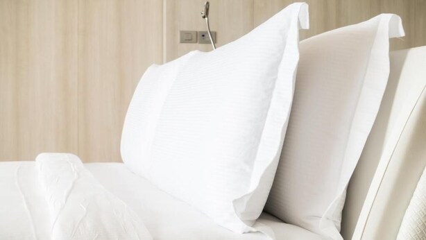 A bed with white linens and pillows, a bedside table, and a wall-mounted power outlet. - Stayspro - Venice Beach Luxury Apartments (Marina del Rey)