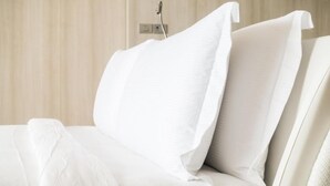 A bed with white linens and pillows, a bedside table, and a wall-mounted power outlet. - Stayspro - Venice Beach Luxury Apartments (Marina del Rey)