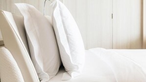 A neatly made bed with white bedding and pillows, a wooden wardrobe in the background, and a door to the right. - Stayspro - Venice Beach Luxury Apartments (Marina del Rey)