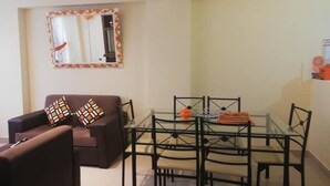 A living room with a brown sofa, two patterned cushions, a glass dining table with chairs, and a decorative mirror on the wall. - Hatun Quilla Apartments (Cusco)