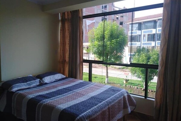 Ein Schlafzimmer mit einem großen Fenster, einem Bett mit einer gestreiften Decke und Vorhängen.