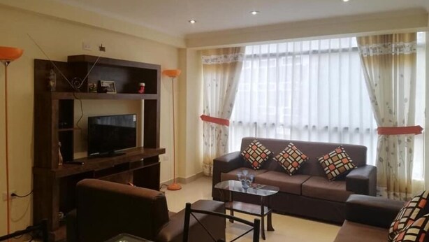 A living room with a sofa, a coffee table, a TV on a wooden stand, and curtains on the windows. - Hatun Quilla Apartments (Cusco)