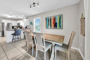Una cocina moderna con armarios blancos, un refrigerador de acero inoxidable y un comedor con mesa y sillas de madera.