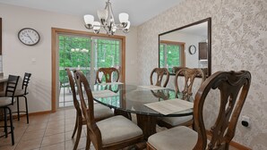 Une salle à manger avec une table en verre entourée de chaises en bois, un lustre et un grand miroir au mur.
