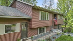 A two-story house with a front porch, a small front yard with a pathway, and an American flag.