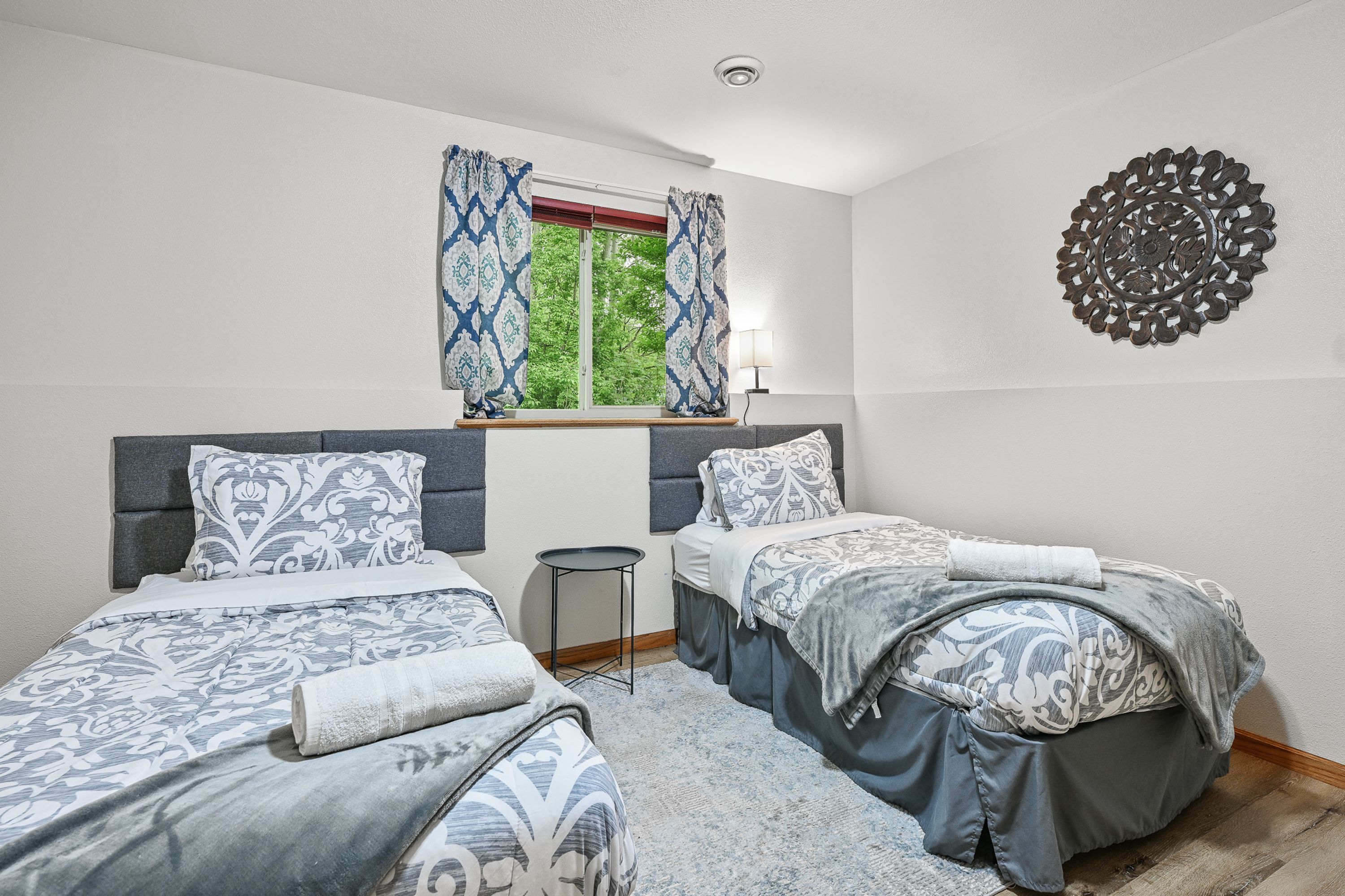 Un dormitorio con dos camas, una ventana con cortinas, una mesita de noche y un adorno en la pared.