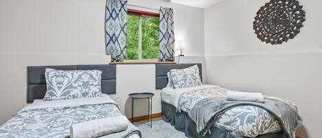 Un dormitorio con dos camas, una ventana con cortinas, una mesita de noche y un adorno en la pared.