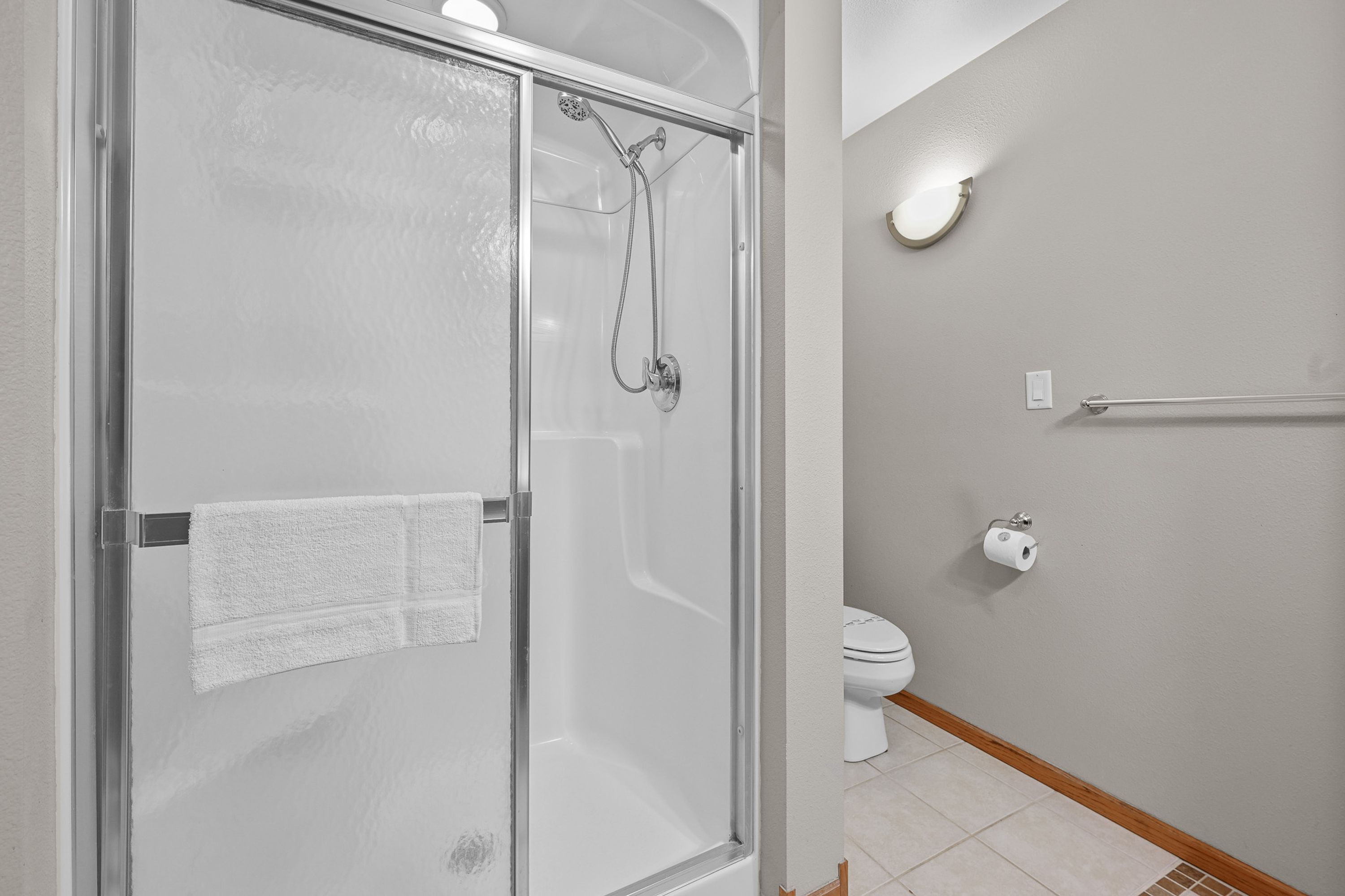 A bathroom with a glass-enclosed shower, a toilet, and a towel rack.