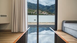 Ein modernes Zimmer mit einem Glastisch, einem grauen Sofa und Blick auf Berge und einen See.