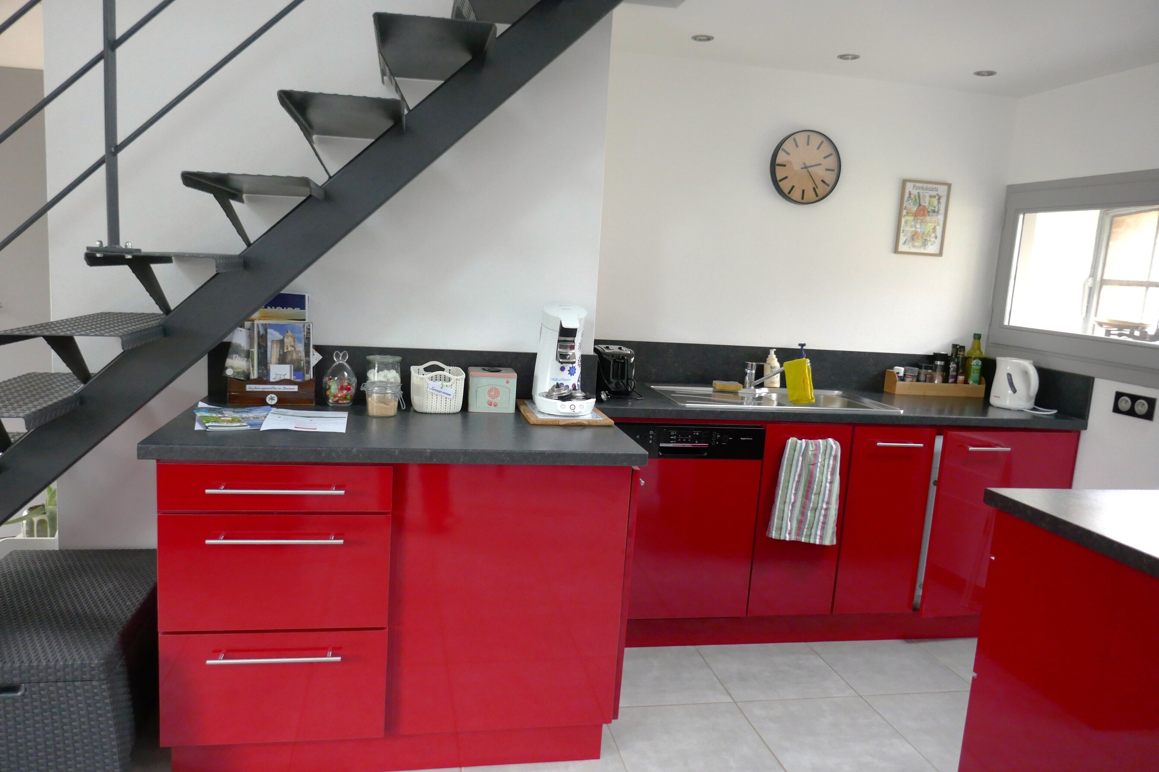 A kitchen with red cabinets, a black countertop, a coffee maker, and a clock on the wall.