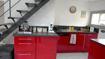 A kitchen with red cabinets, a black countertop, a coffee maker, and a clock on the wall.