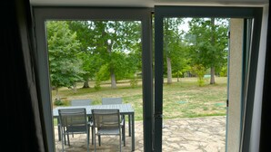 A patio with a table and chairs, a stone floor, and a view of a grassy area with trees. - Country house at the gateway to the Limousin-Périgord nature park. (Rilhac-Lastours)