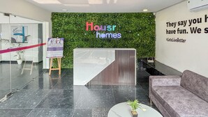 Un área de recepción moderna con una pared verde, un mostrador de recepción, un sofá y un letrero que dice "Housr homes".