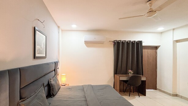 Un dormitorio con cama, mesita de noche, lámpara, escritorio, silla y ventilador de techo.