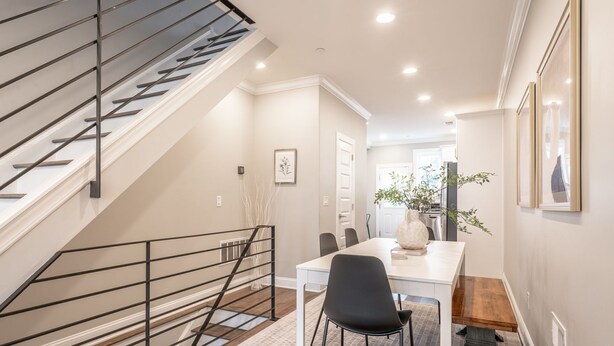Een modern interieur met een trap, een eetgedeelte met een witte tafel en zwarte stoelen, en een gang naar een andere kamer.