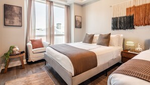 Een moderne hotelkamer met een groot bed, een zithoekje, een nachtkastje en uitzicht op de stad.