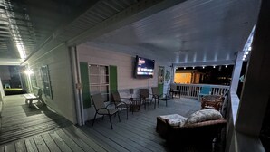 A covered outdoor area with wooden flooring, chairs, and a television screen.